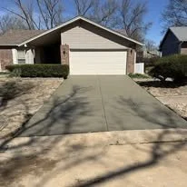 Front view of a house with a concrete driveway, small front yard, bushes, and trees, in a suburban neighborhood