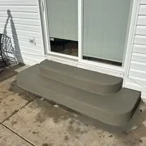 A gray plastic pet step stool with two steps placed outside a sliding glass door on a concrete surface.