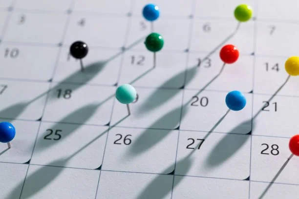 Calendar with colorful push pins marking dates and casting shadows.