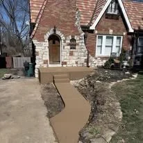 A newly built concrete sidewalk leading to the front door of a brick house with stairs and porch.