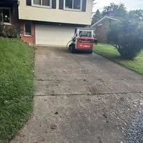 A driveway in front of a house with a garage, with a red and white vehicle parked on it, and a grassy lawn on either side.
