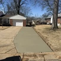 Freshly poured concrete sidewalk in a suburban neighborhood with houses, trees, and grass on either side.