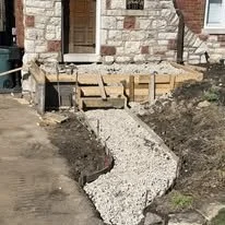 New gravel pathway with wooden steps leading to a stone house entrance.