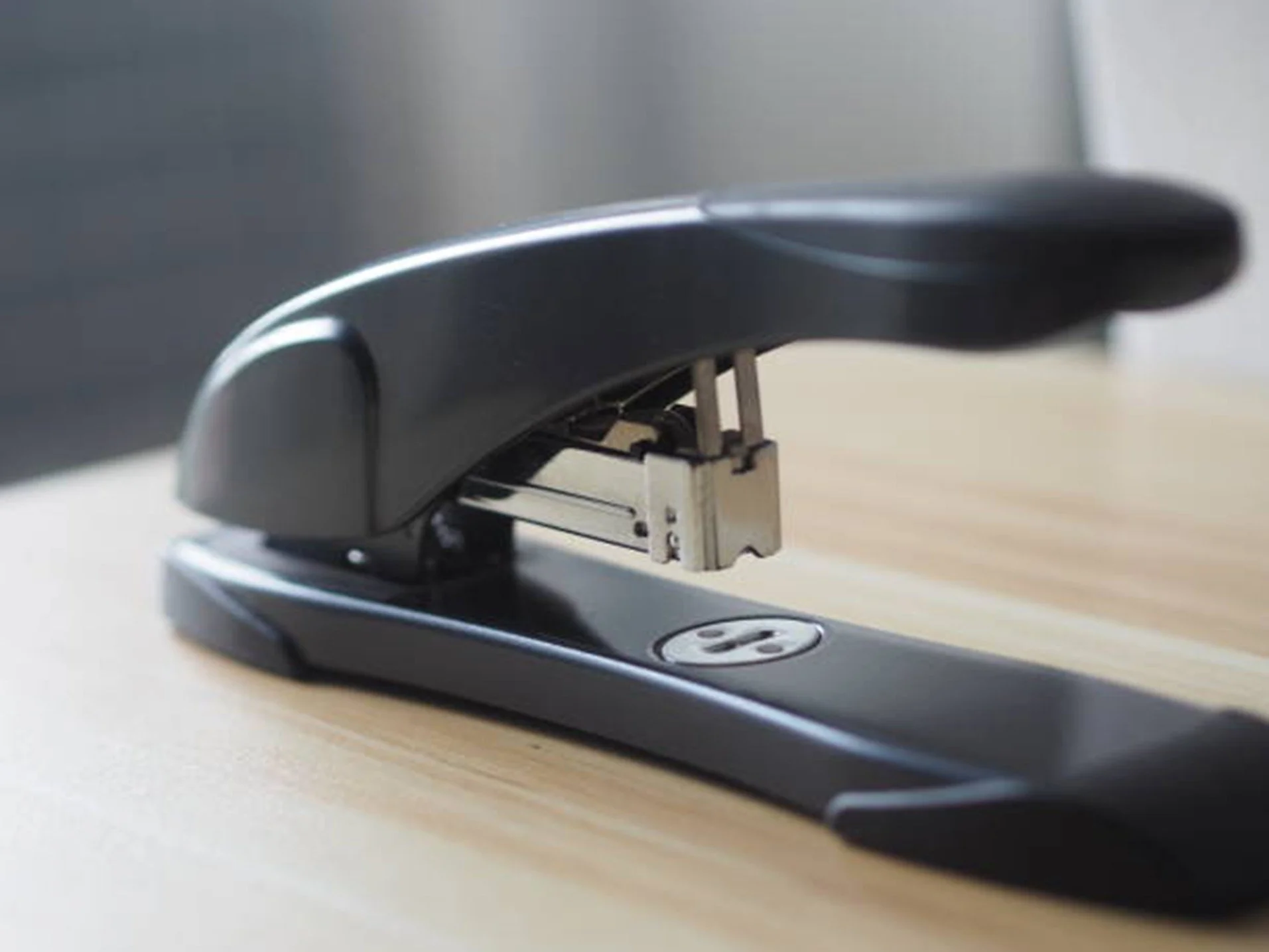 Close-up of a black stapler on a wooden desk with a blurred background.