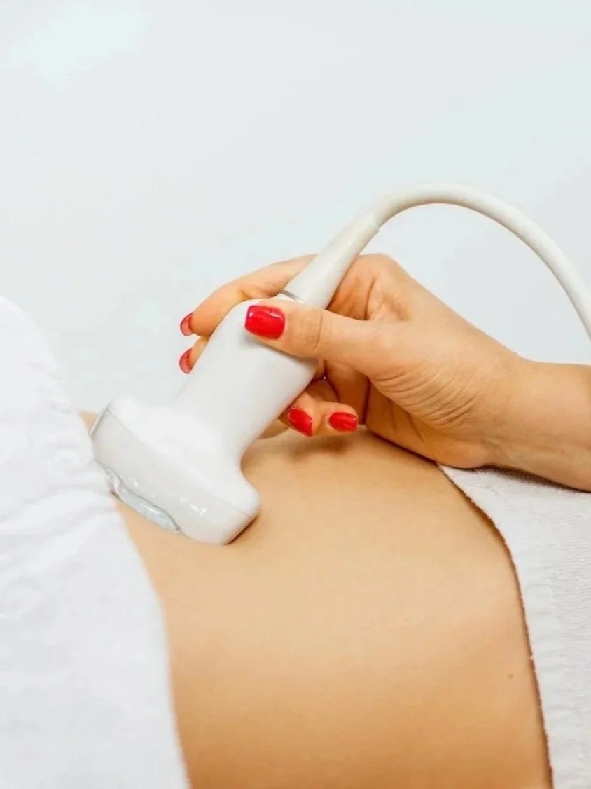 A person receiving an ultrasound on their abdomen, with the ultrasound probe held by someone with red-painted nails.