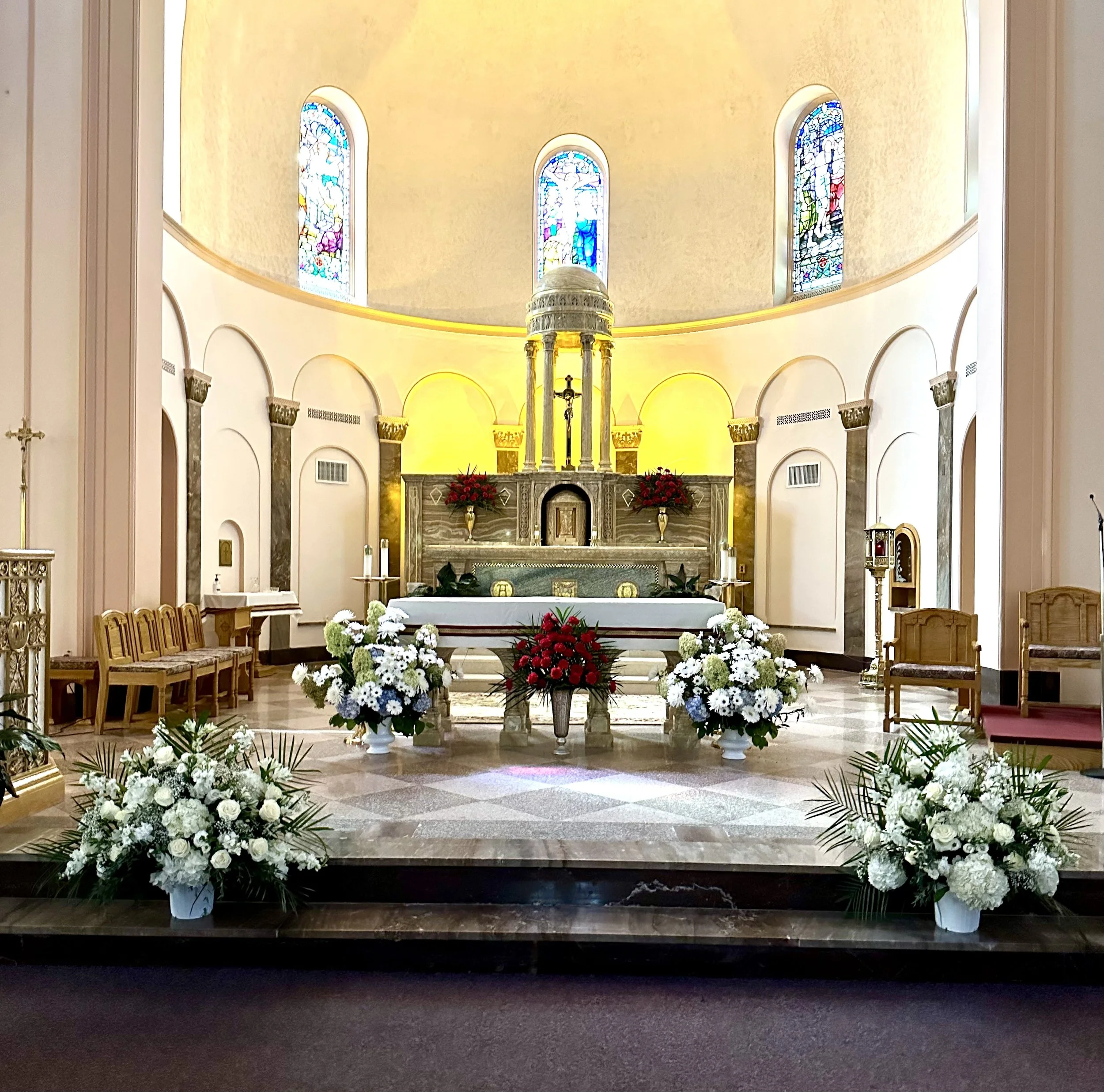The interior of a church or chapel with an altar decorated with flowers, stained glass windows, and religious artifacts.