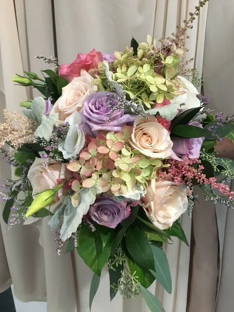 A bouquet of various flowers including roses, hydrangeas, and greenery in pastel colors.