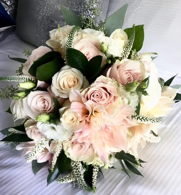 A bouquet of pink and white roses, roses, and greenery on a bed.