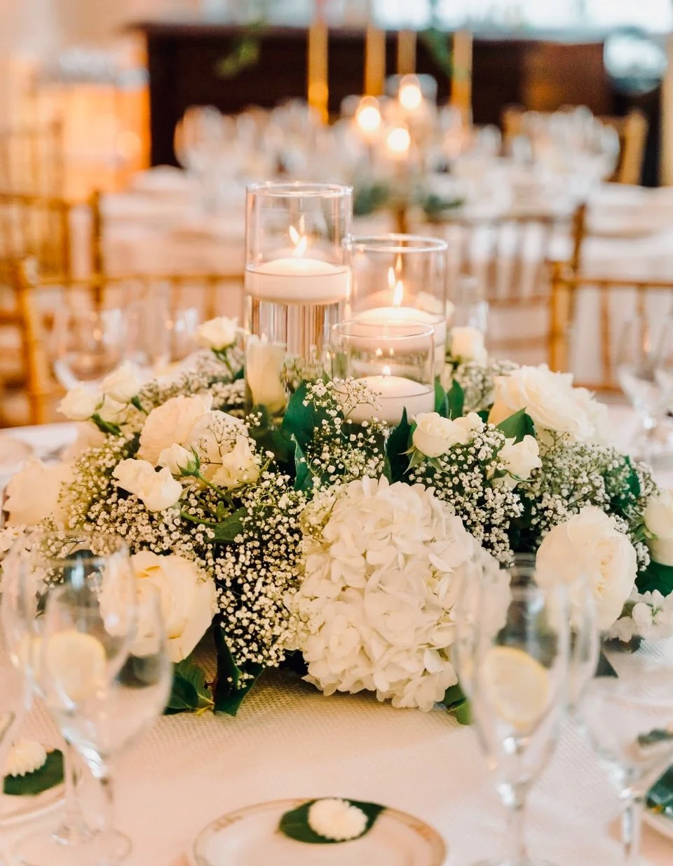 Elegant table centerpiece with white flowers and floating candles in glass holders at a formal event.
