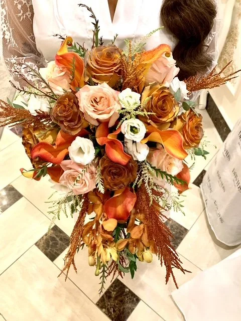 A cascading bridal bouquet with roses, calla lilies, and greenery with a person in white holding it.