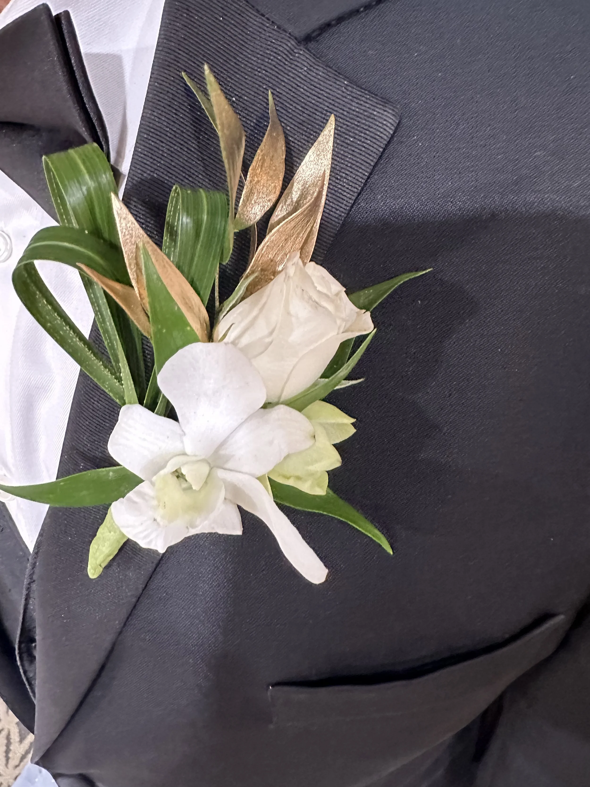 A floral corsage with white flowers and green leaves on a black surface.