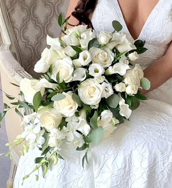 A woman in a white dress holding a cascading bouquet of white roses and greenery.