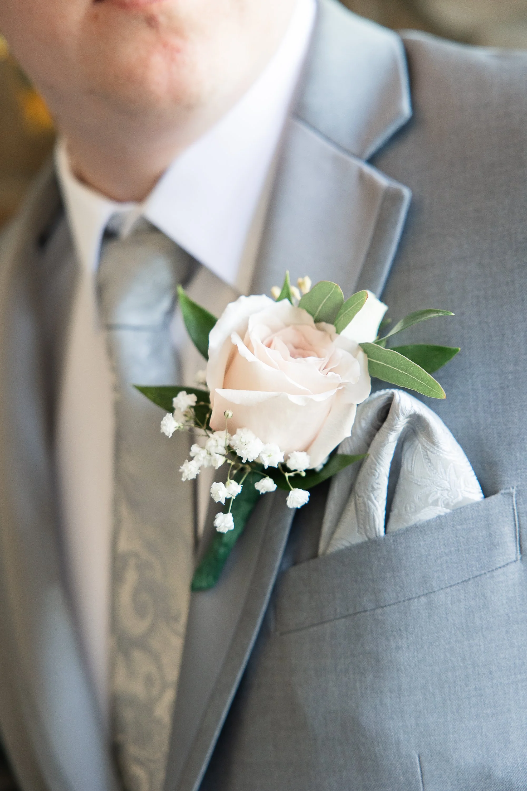 Close-up of a man's suit with a boutonniere featuring a white rose and green leaves on the lapel.