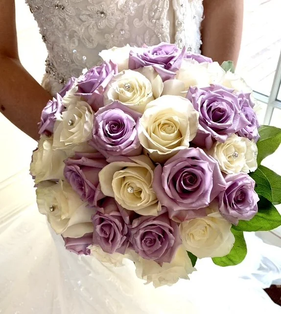 A bride holding a bouquet of large, pastel-colored roses in shades of white and lavender, accented with green leaves.