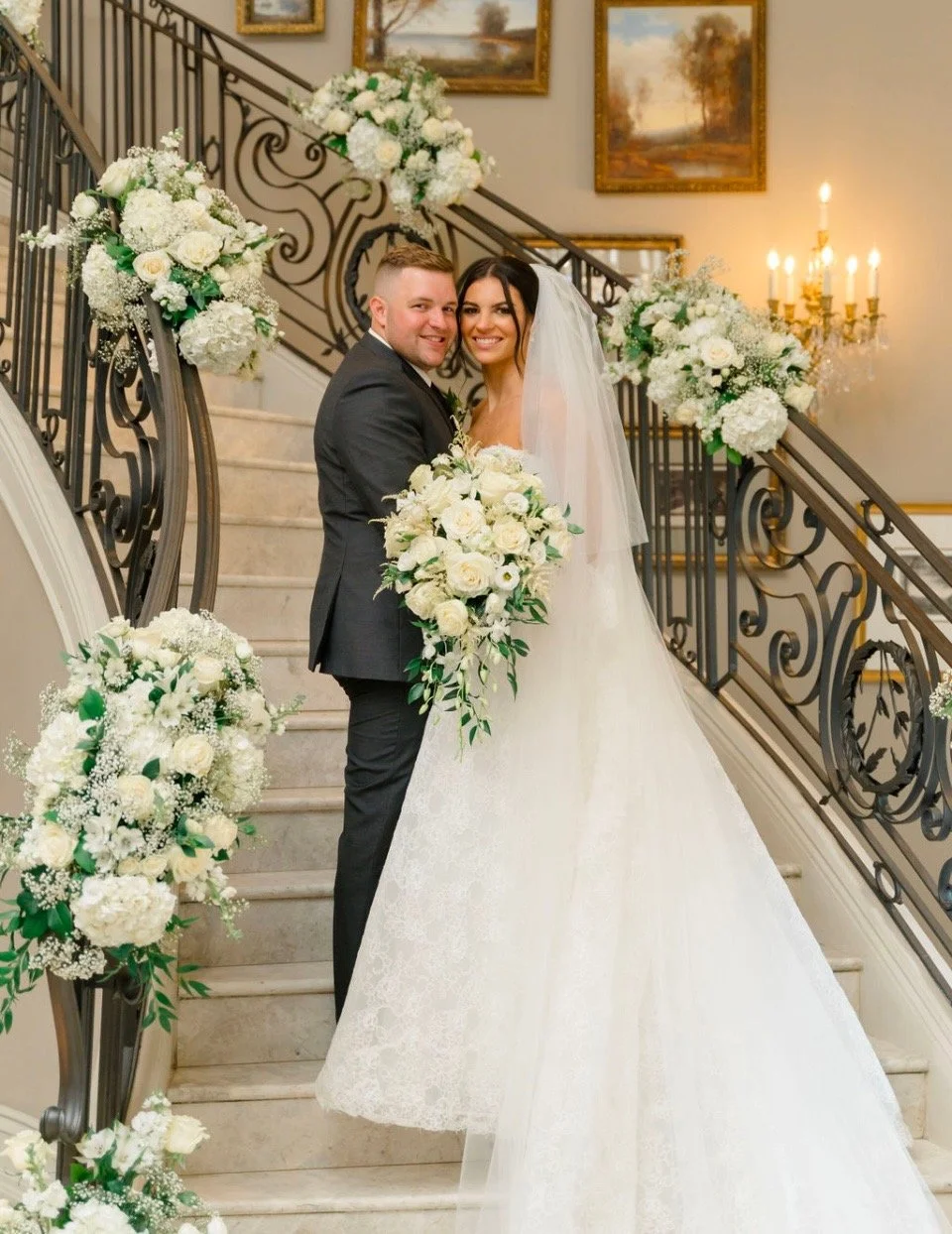 A newlywed couple stands on a staircase decorated with white floral arrangements, celebrating their wedding.