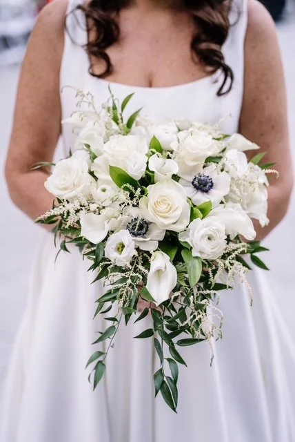 Bride holding a bouquet of white roses, calla lilies, and greenery at her wedding.