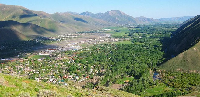 A valley with a small town, surrounded by green hills and mountains under a blue sky.