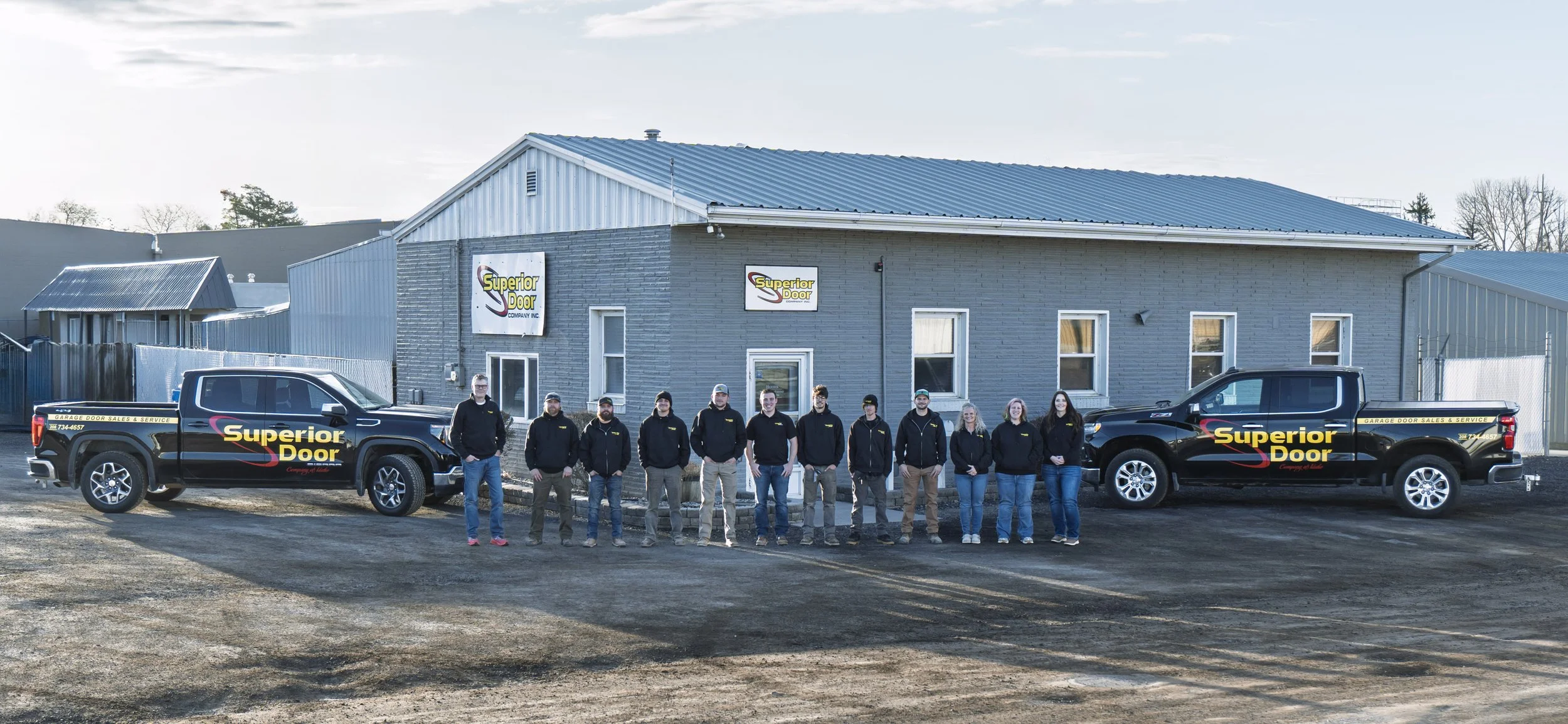 Group of people standing in front of a building with two trucks branded 'Superior Door'.