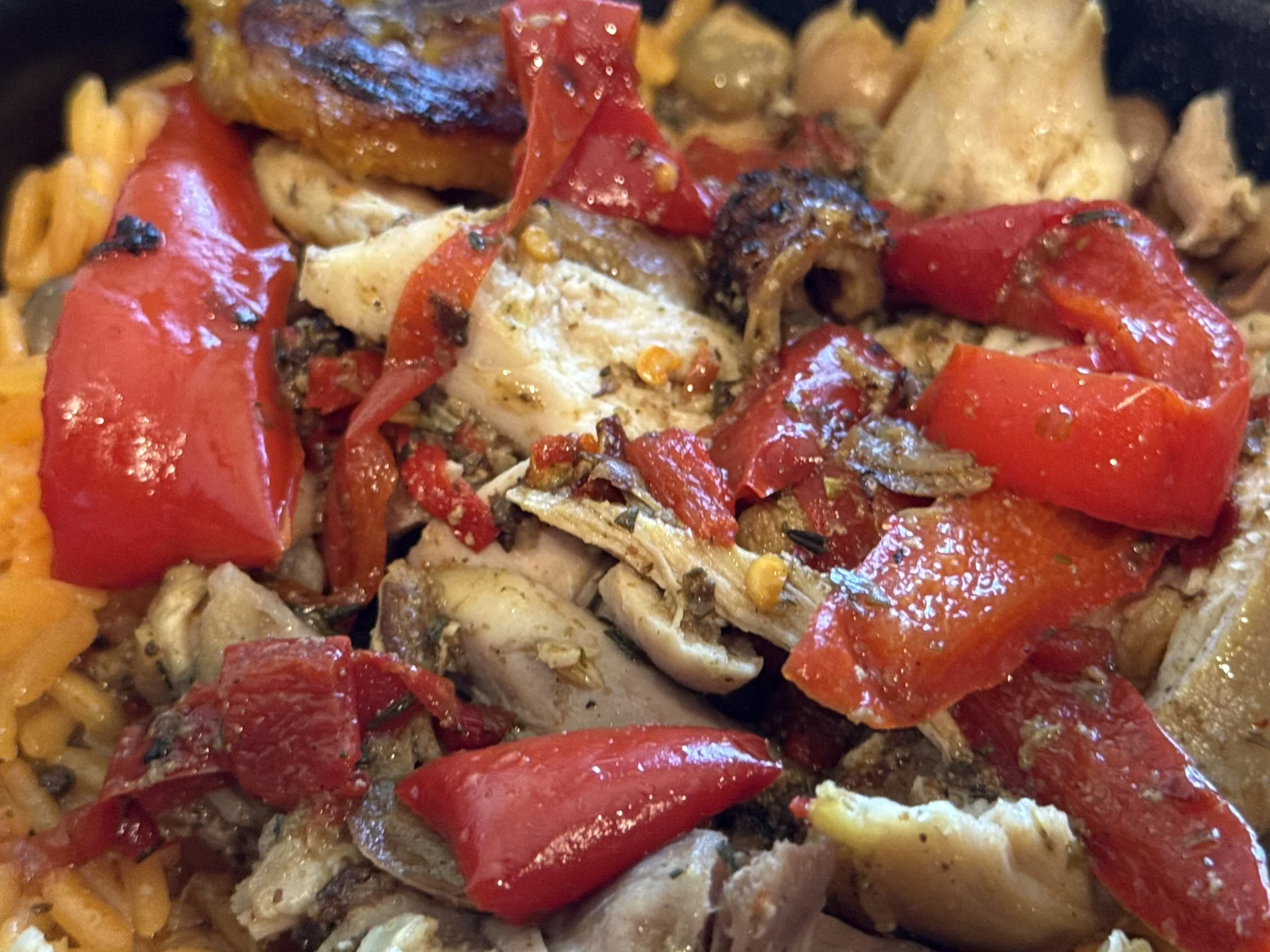 Close-up of a dish with red bell peppers, shredded chicken, and cooked rice, garnished with herbs.