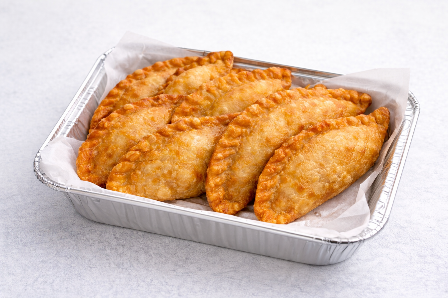Five cooked, breaded chicken fried steaks in a disposable aluminum tray lined with parchment paper.