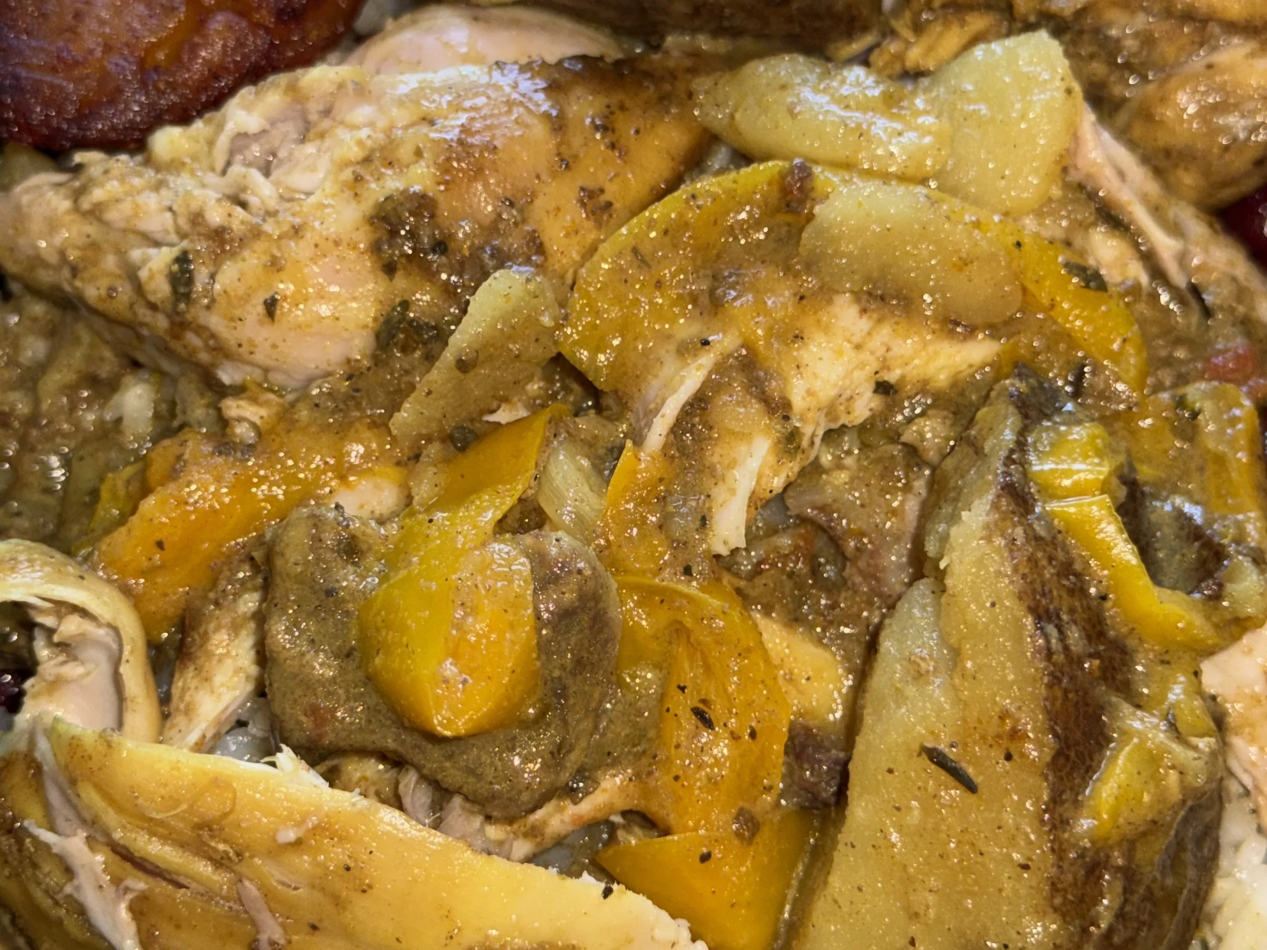 Close-up of food featuring chicken, potatoes, spices, and herbs, with some fried food in the upper left corner.