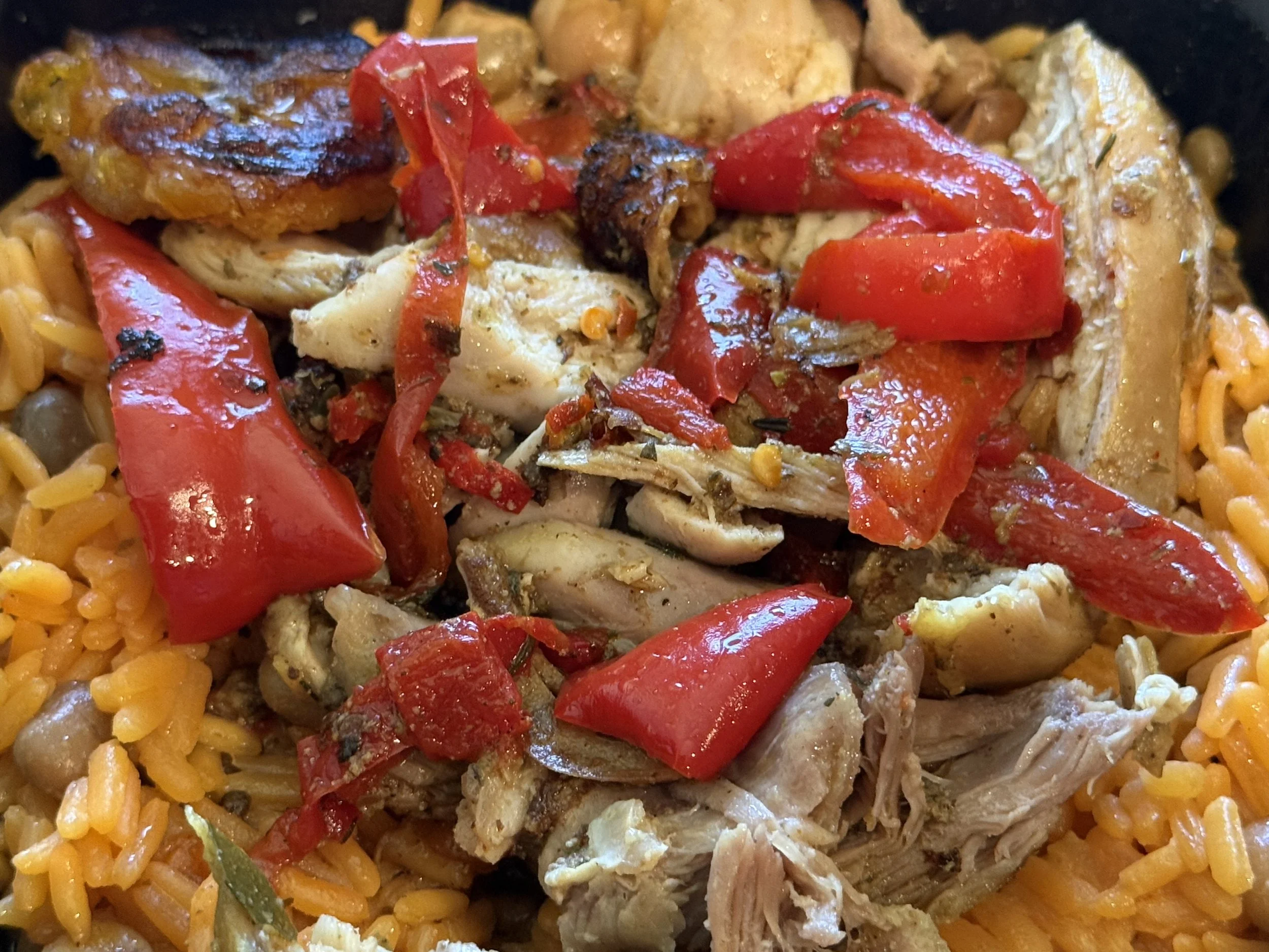 Close-up of cooked shredded chicken, red bell pepper pieces, and yellow rice with beans.