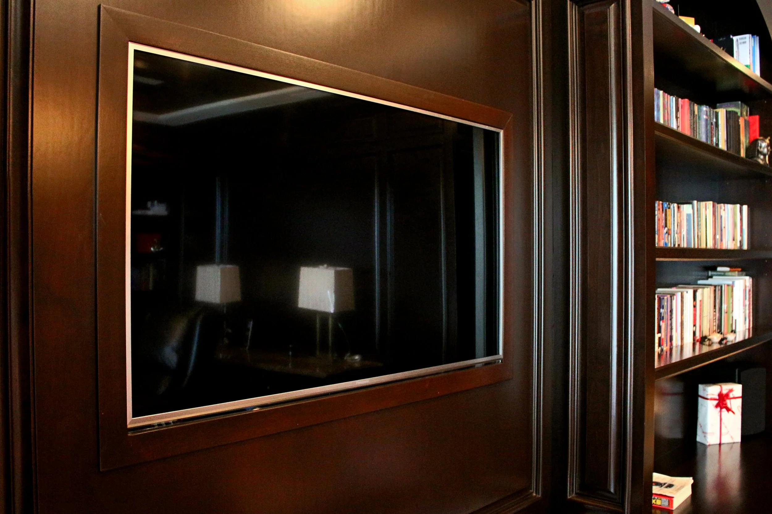 A dark wooden entertainment center with a large empty space for a television, next to a bookshelf filled with colorful books and a small black figurine.