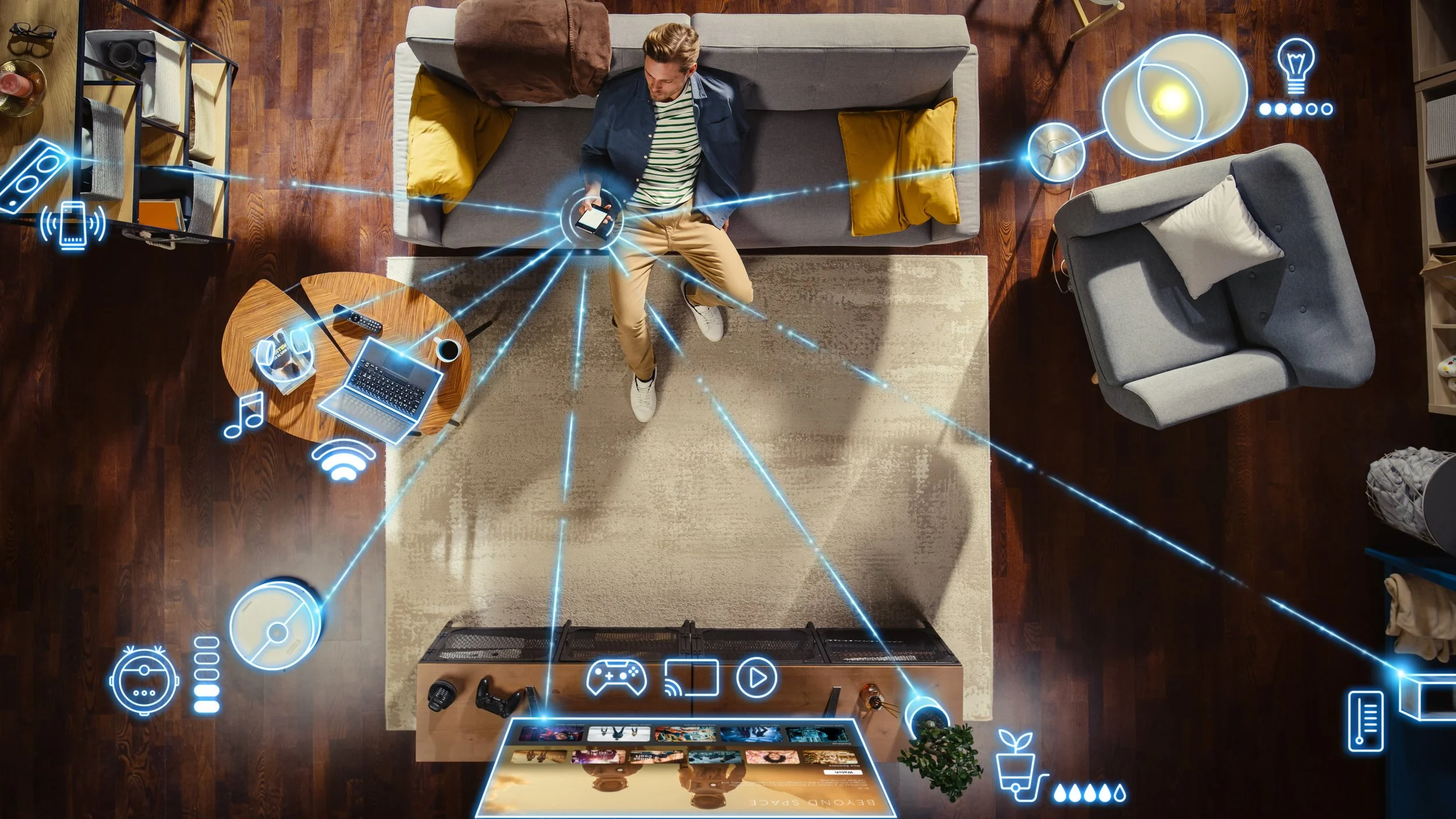 A man sitting on a gray sofa looking at his phone in a living room with smart home icons overlayed, indicating connected devices such as a speaker, lights, and electronics.