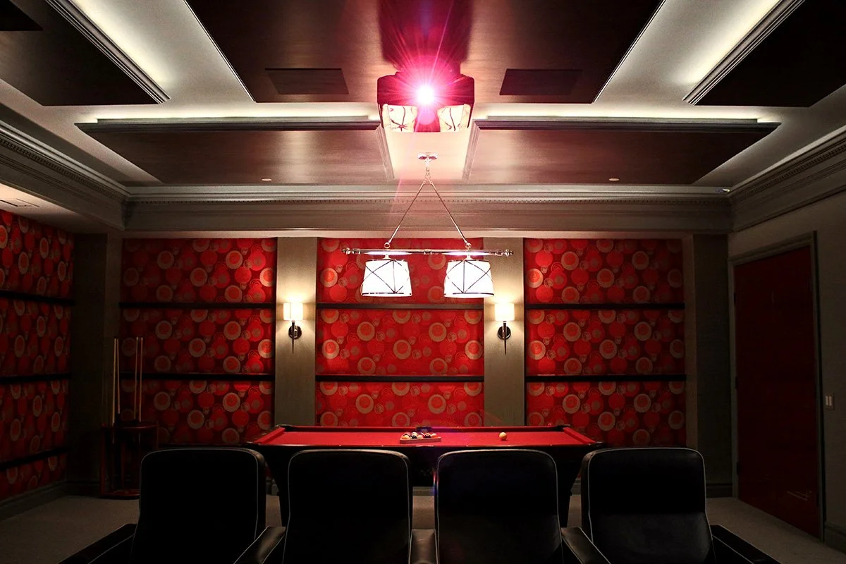 A dimly lit game room with a pool table, red patterned wallpaper, wall-mounted lights, and a ceiling light fixture.