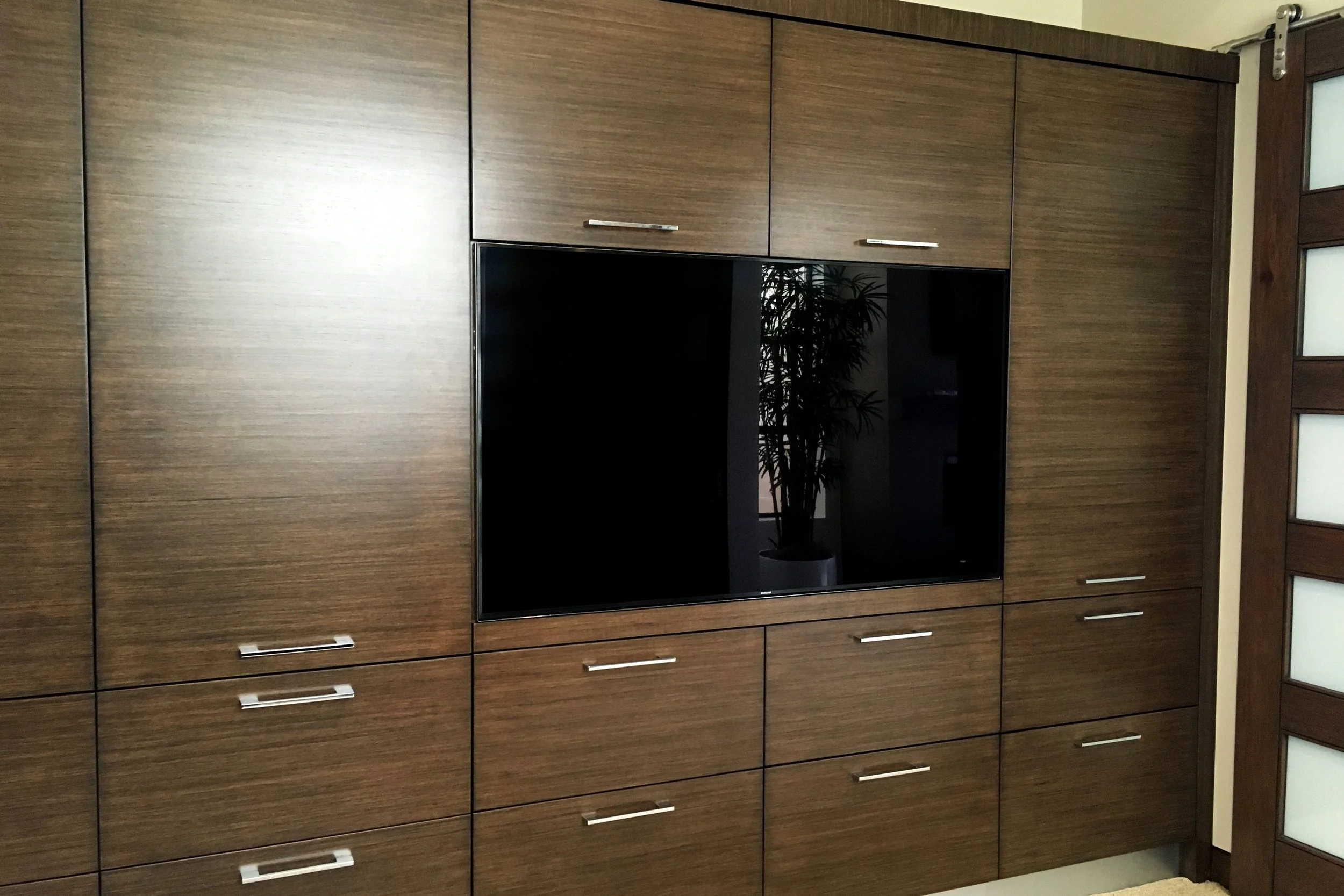 Wooden cabinet with multiple drawers and a flat-screen TV in the center, reflected in the glass door of a neighboring cabinet.