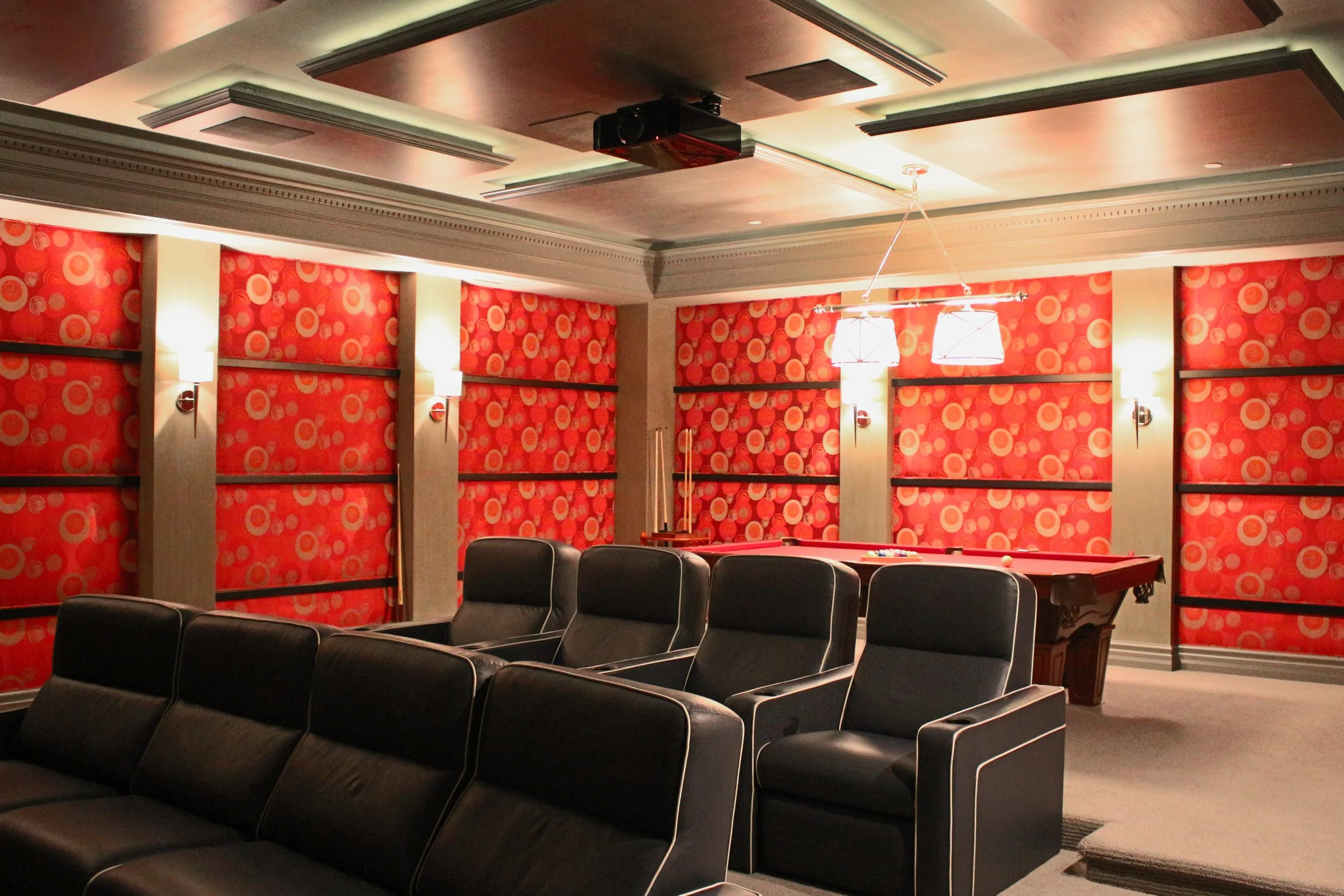 A room with red patterned walls, black chairs, a pool table, and ceiling lights.