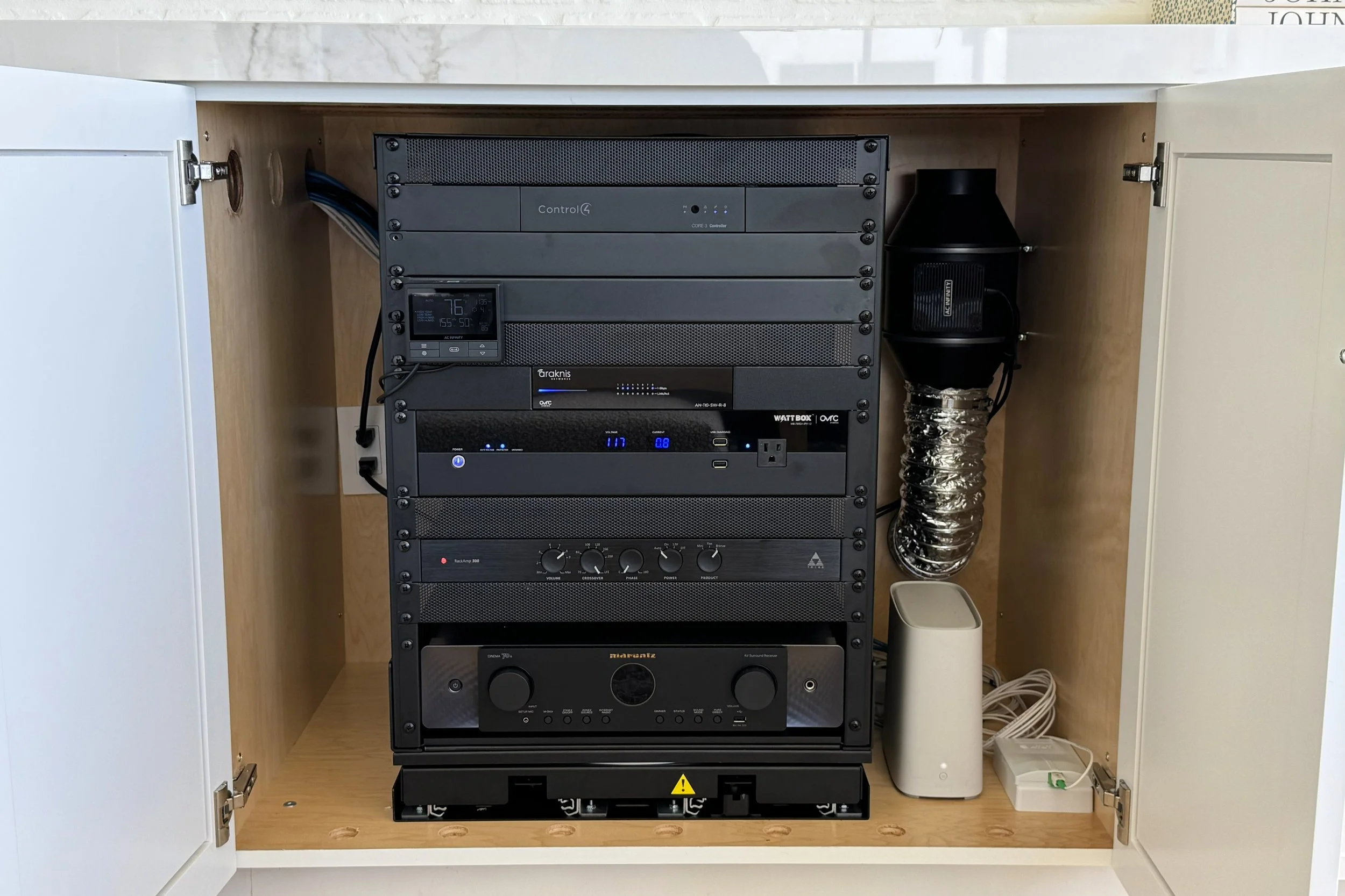 Inside a wooden cabinet with electronic equipment including a control4 device, a digital thermostat showing 76 degrees, an amplifier, a ventilation duct, and various cords and cables.