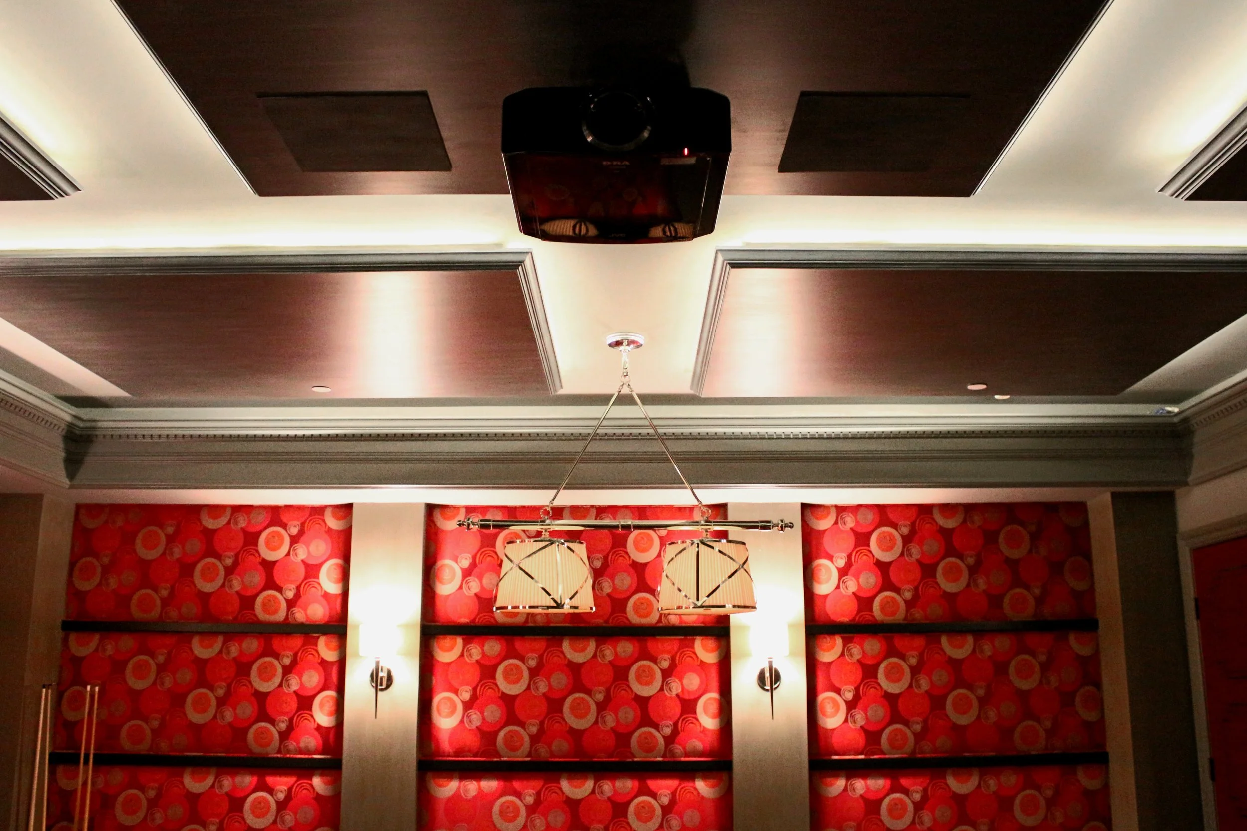 Ceiling with dark wood panels, a black projector, two decorative hanging lights, and a patterned red wallpaper with circular designs.