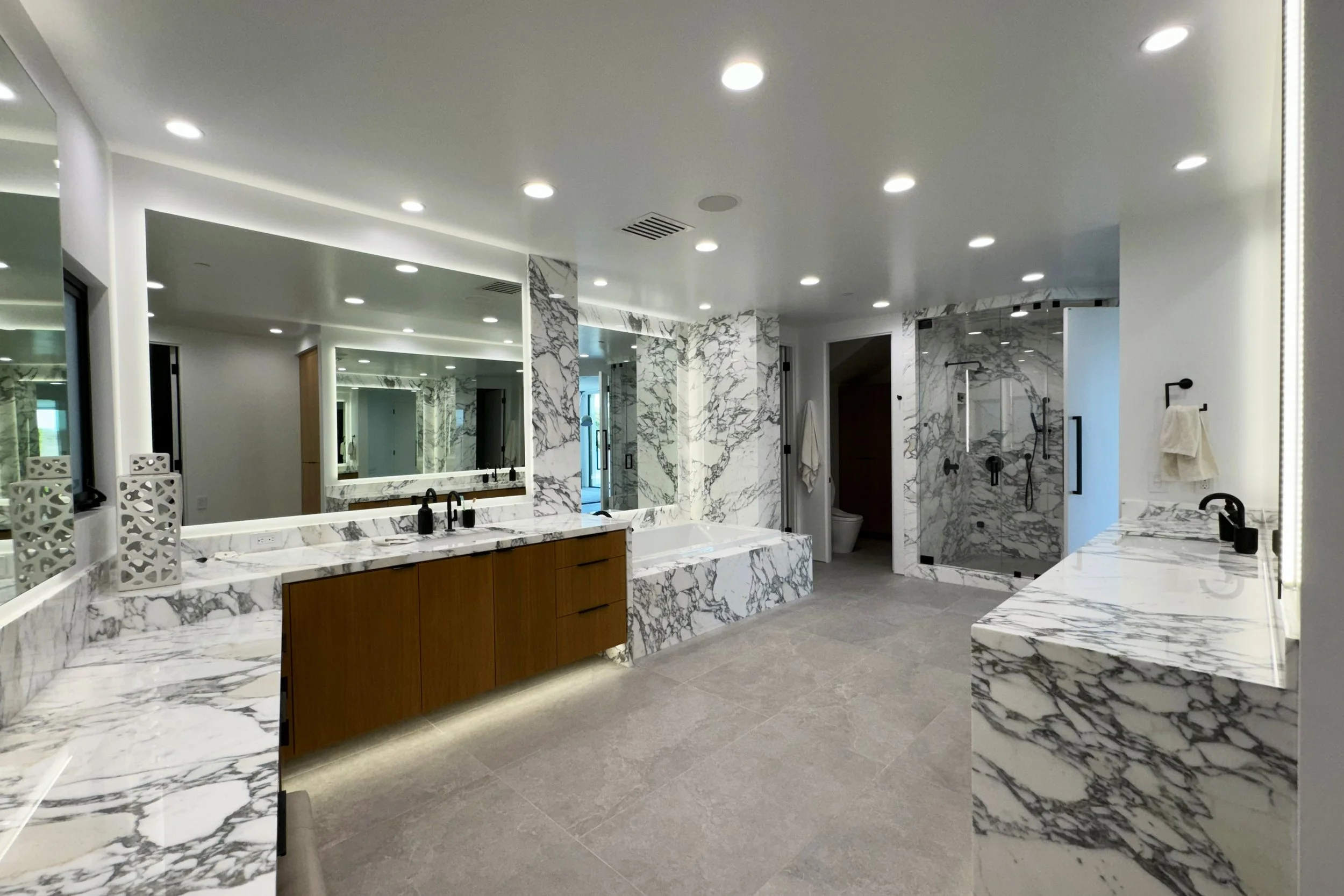 Modern bathroom with marble countertops, a large mirror, and a walk-in shower with glass door.