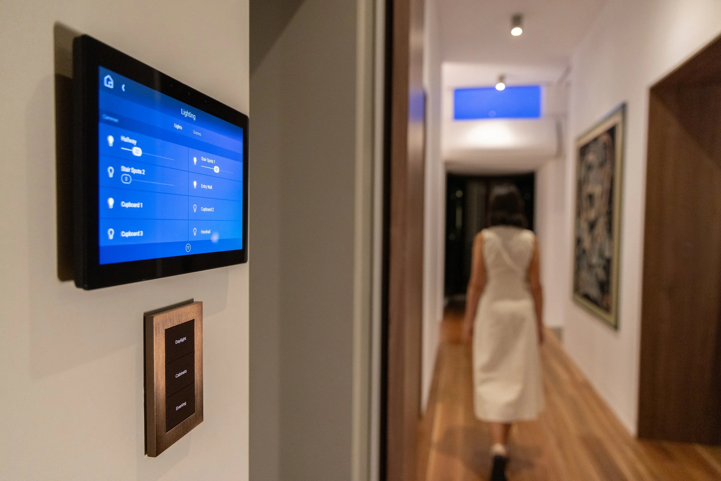 Smart home control panel on a wall showing lighting settings in a hallway of a modern home