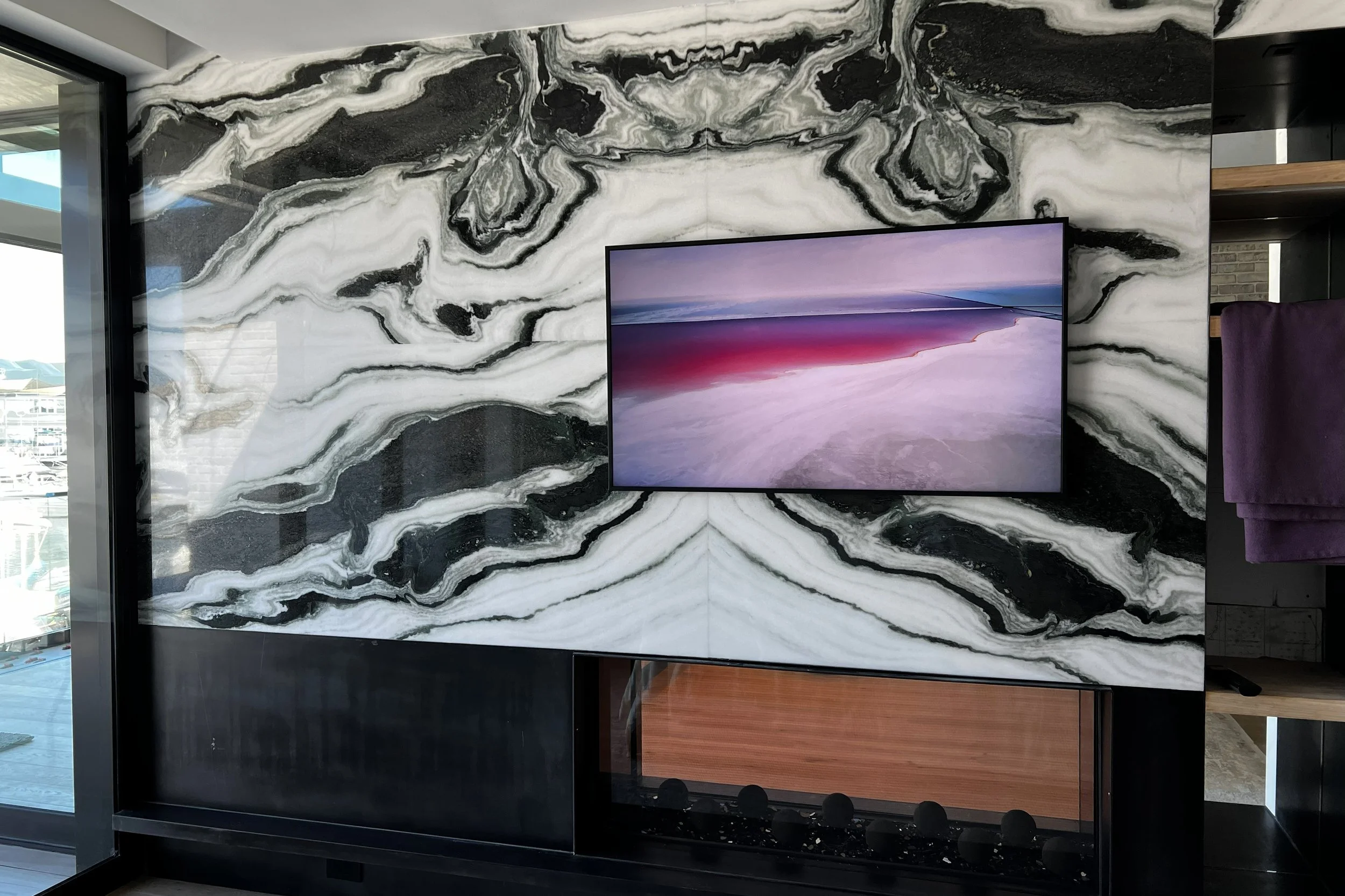 Interior with a large black and white marble wall, a flat-screen television displaying a landscape, and a purple chair visible on the right side.