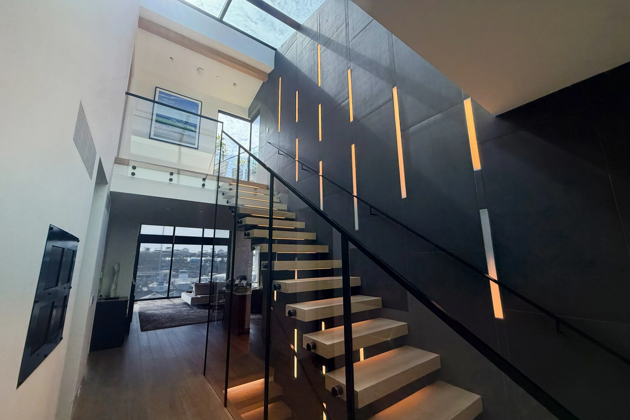 A modern staircase with wooden steps and a black metal railing inside a building with large windows and dark accent walls.