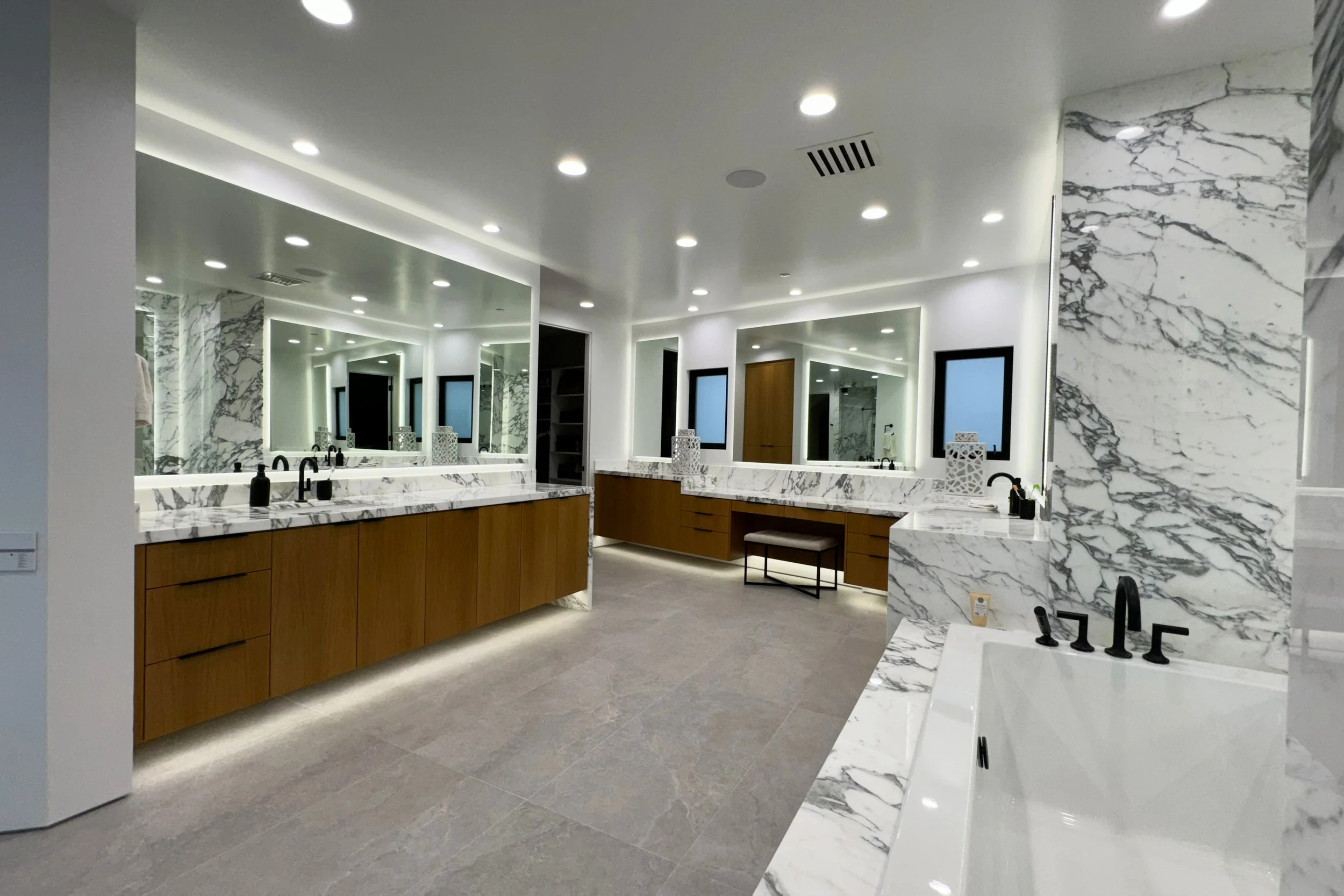 Modern bathroom with marble walls and countertops, wooden vanities, and recessed lighting.