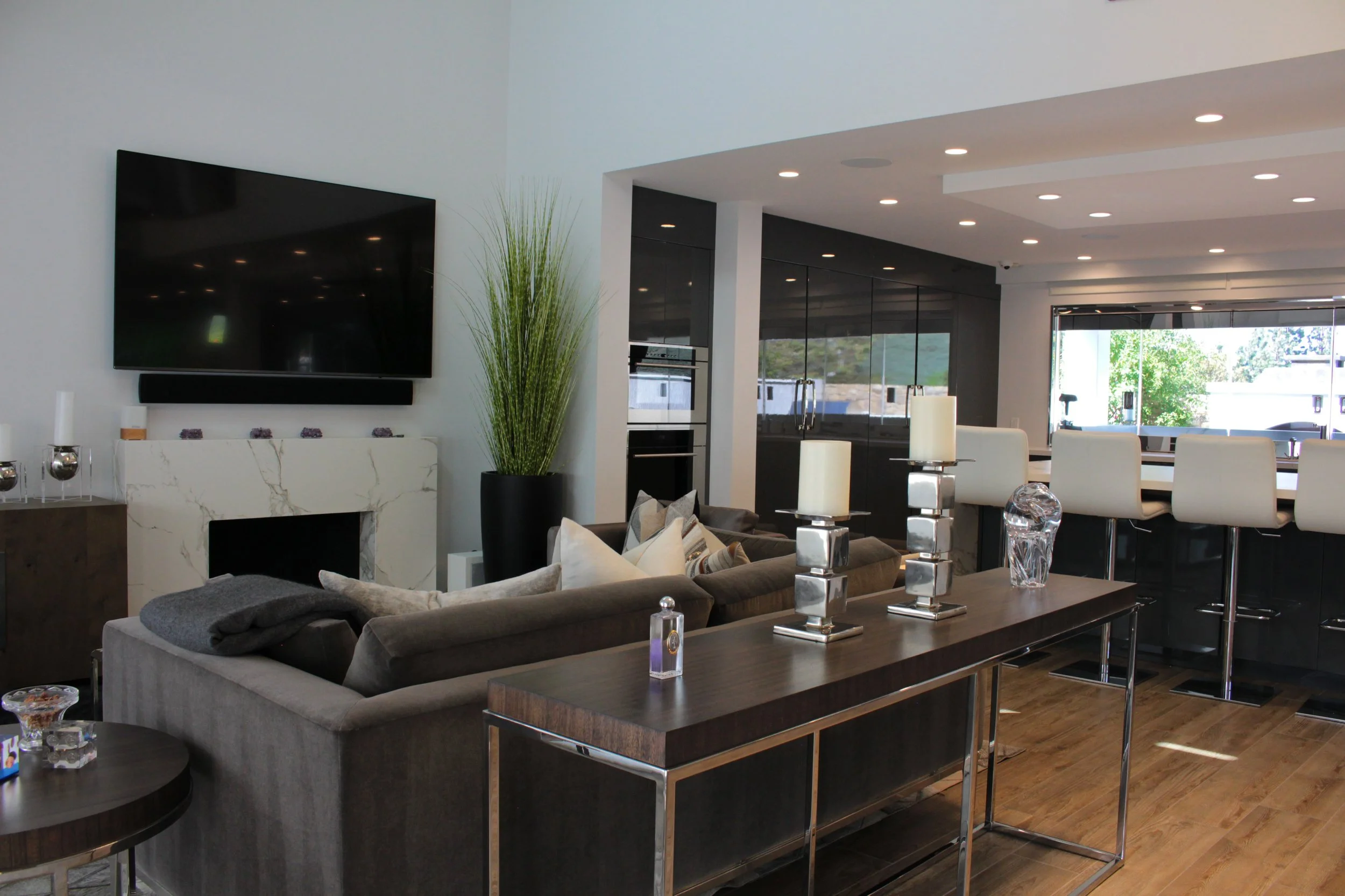 Modern open-concept living room and kitchen with white walls, large window, dining table, chairs, sofa, fireplace, and decorative items.