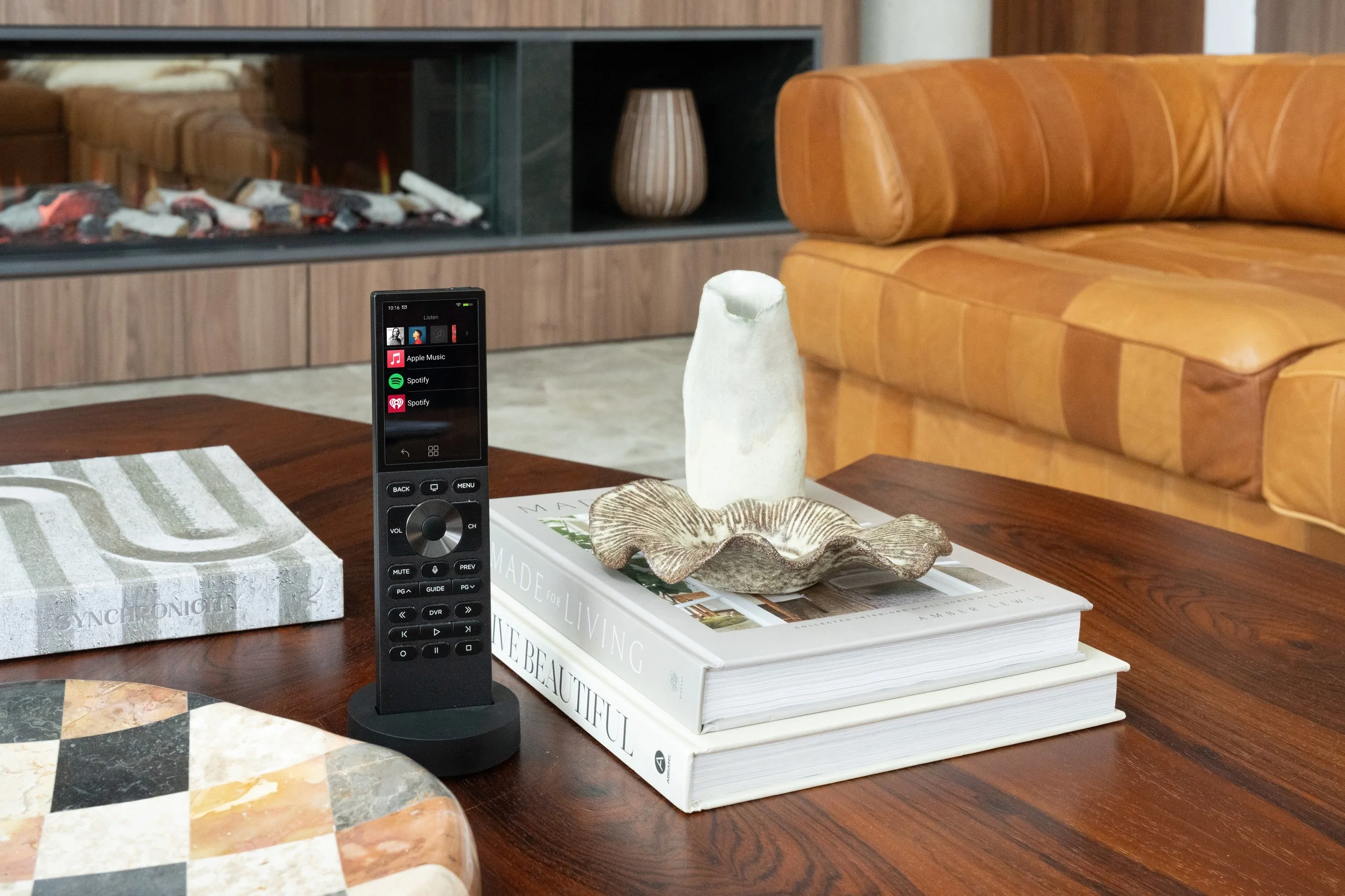 Living room with a wooden table, books, decorative shell, remote control, lit fireplace, orange sofa, and a ceramic vase.