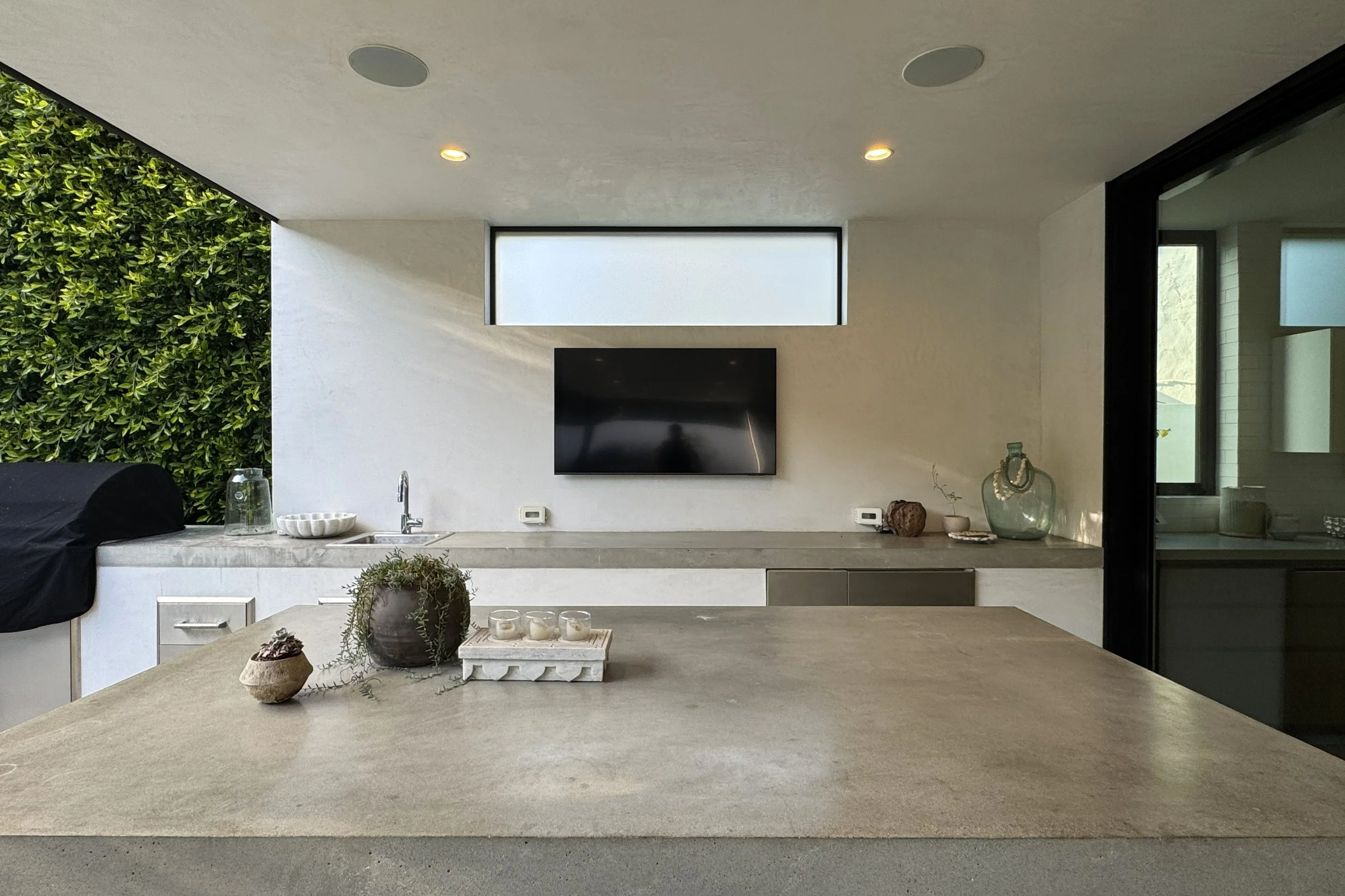 Modern kitchen with a concrete countertop, decorative items, a large window, and a mounted flat-screen TV on the wall.