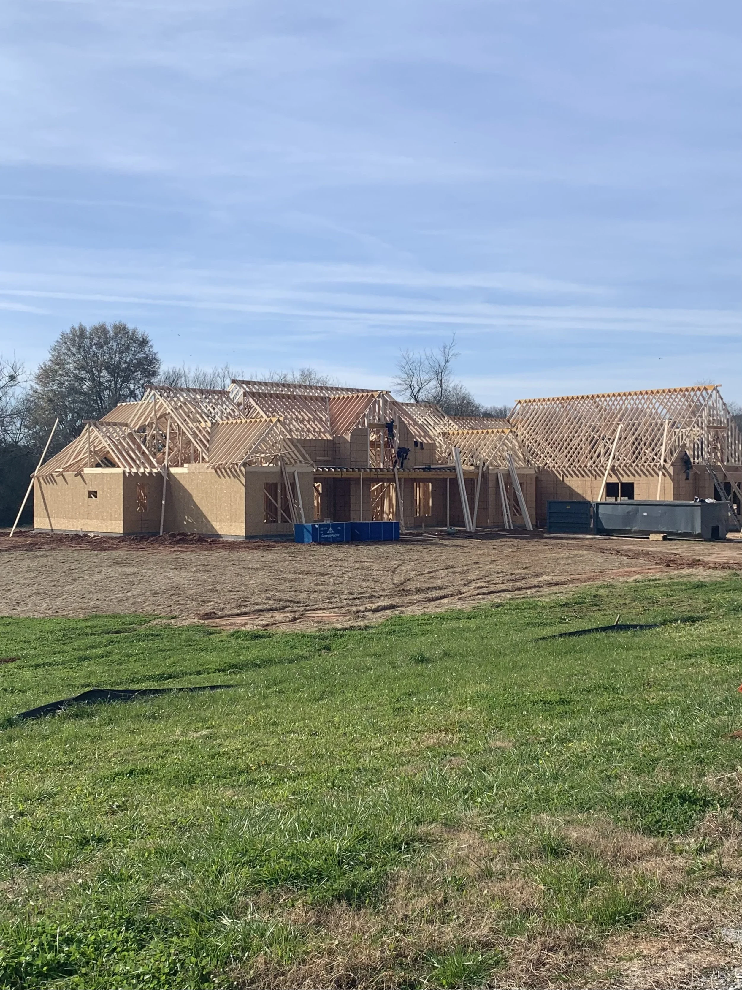 Construction site with wooden framing of a house, partially built, under clear blue sky.