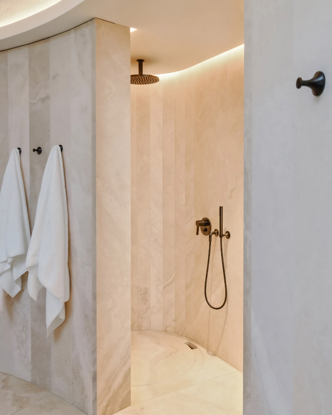 Modern bathroom with white brick walls, black and white patterned floor tiles, a wall-mounted sink with a wooden cabinet, a mirror, potted plants on shelves, and a shower with a glass partition.