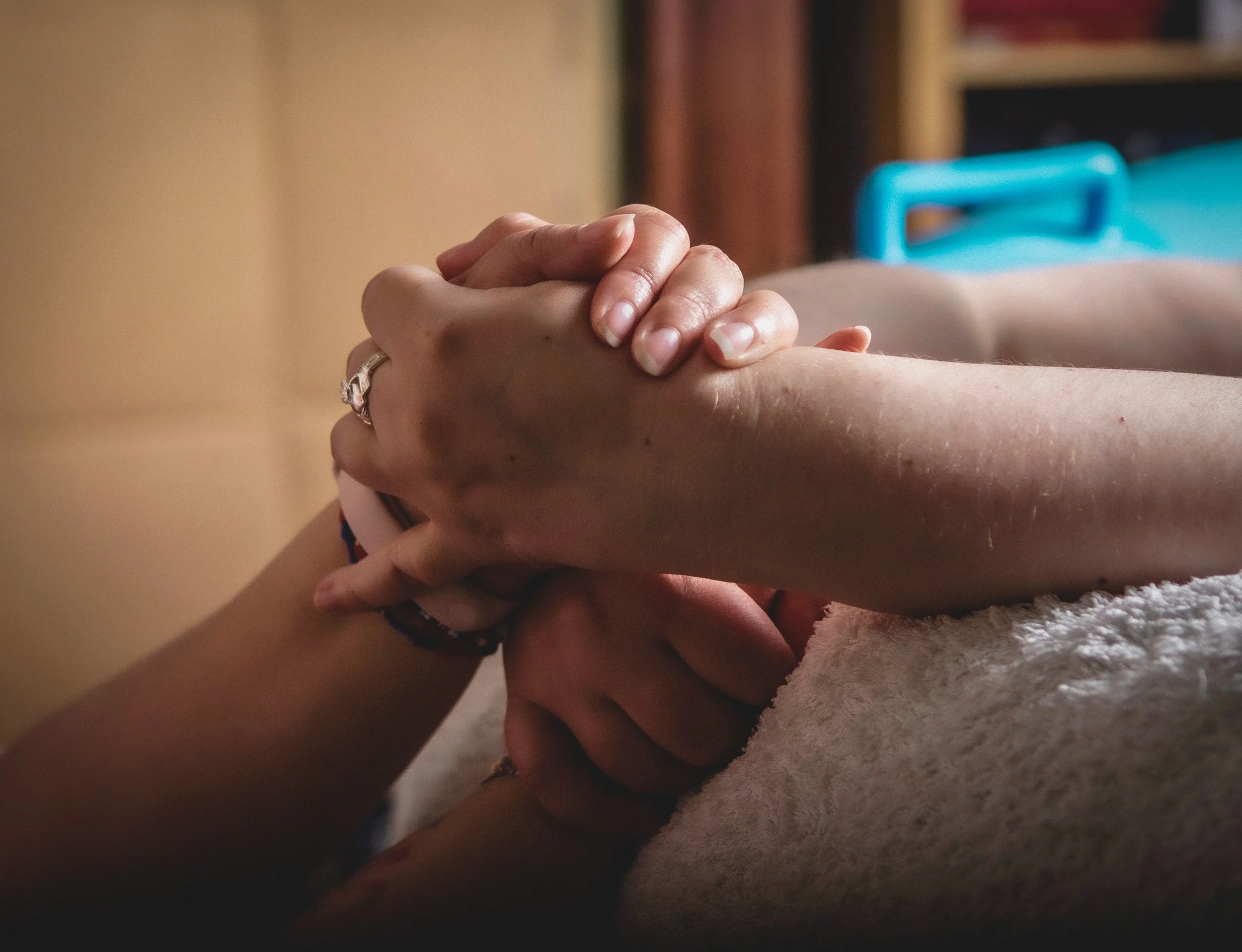 Close-up of two pairs of hands interlocked in a supportive grip, resting on a soft white towel during labour.
