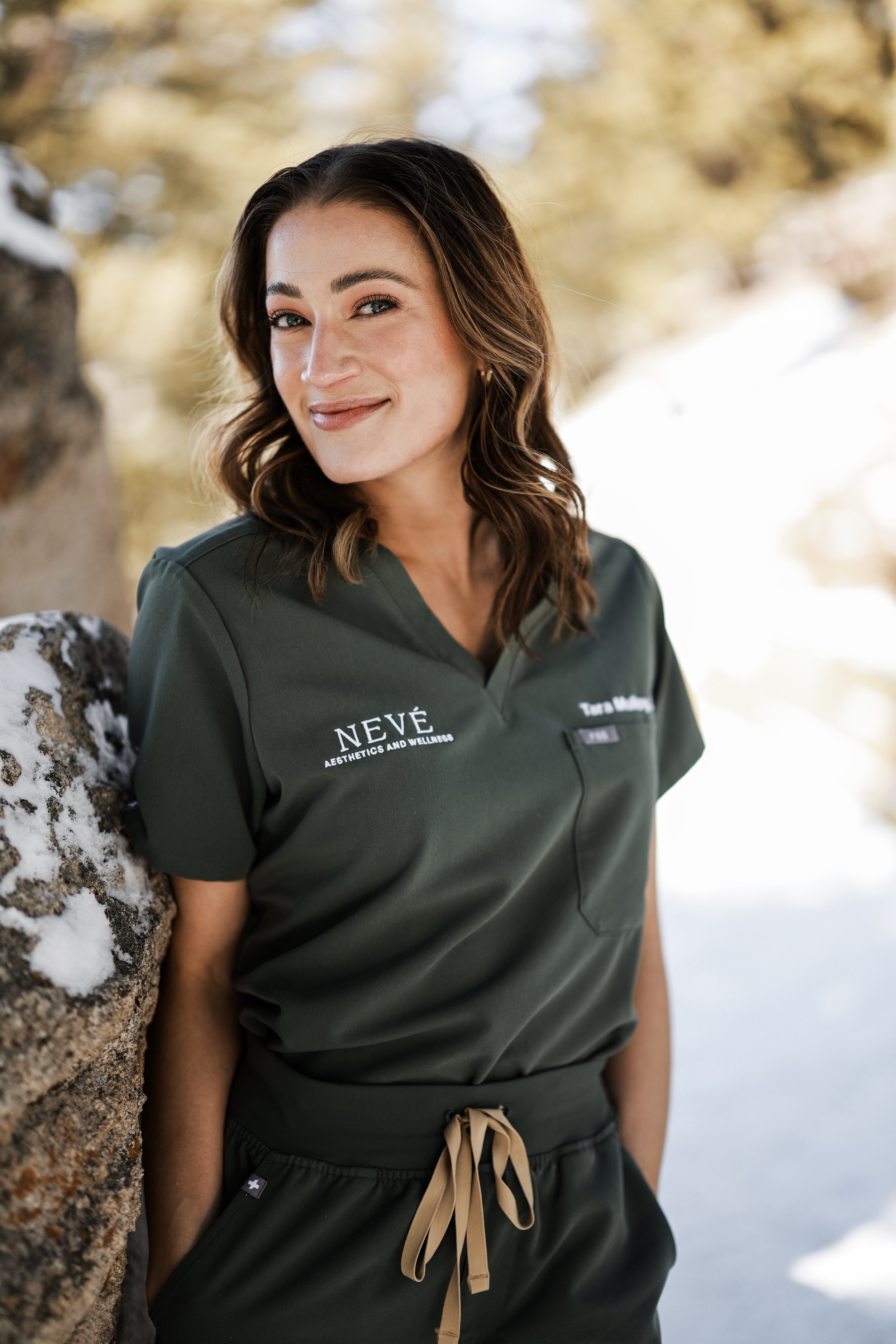provider with brown hair in scrubs outside with springtime mountain scenery