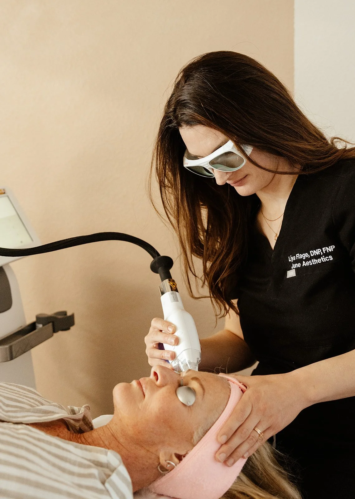provider in black scrubs wearing protective goggles treating a patient with a laser for skin health