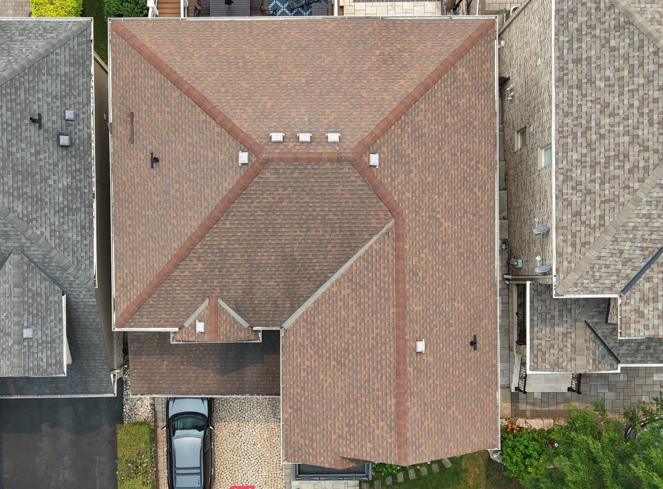 Top-down aerial view of multiple houses with different colored roofs, driveways, and parked cars in a suburban neighborhood.