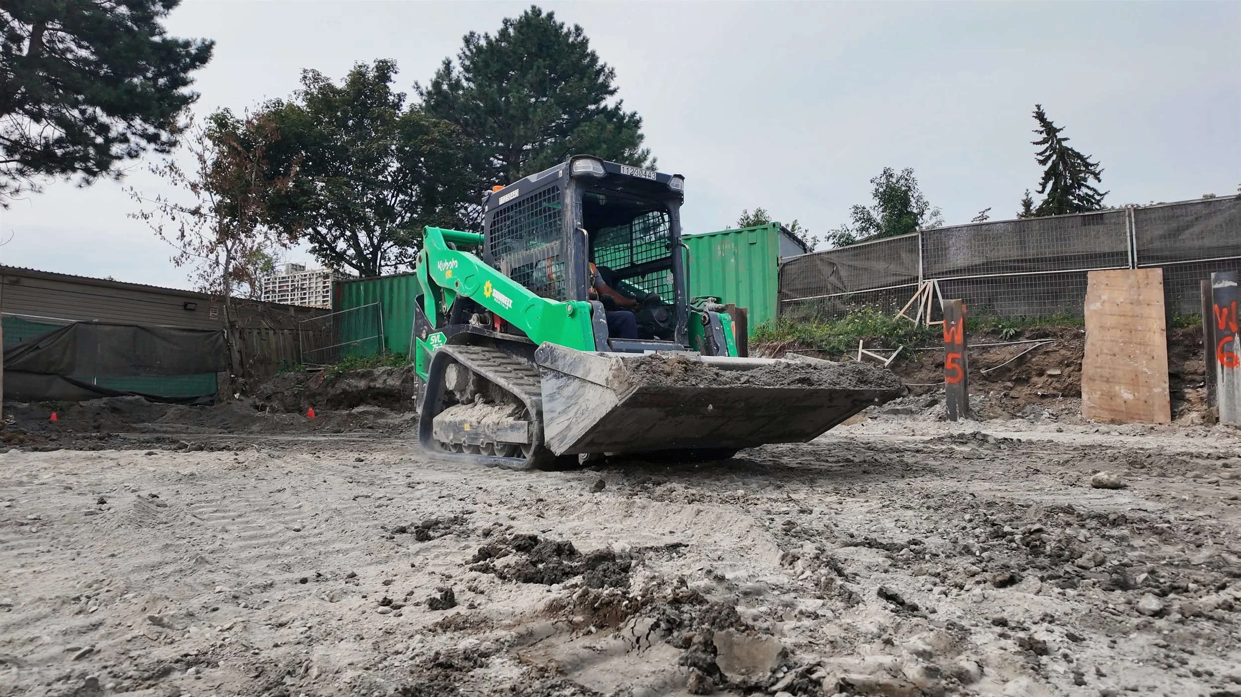 A small green bulldozer moving dirt on a construction site surrounded by trees and construction barriers.