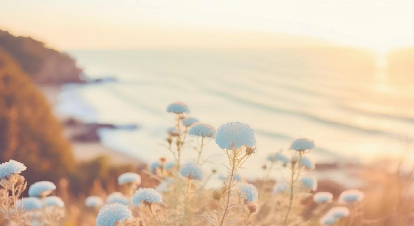 Blurred view of blue flowers on a coast during sunset with hills and ocean in the background.