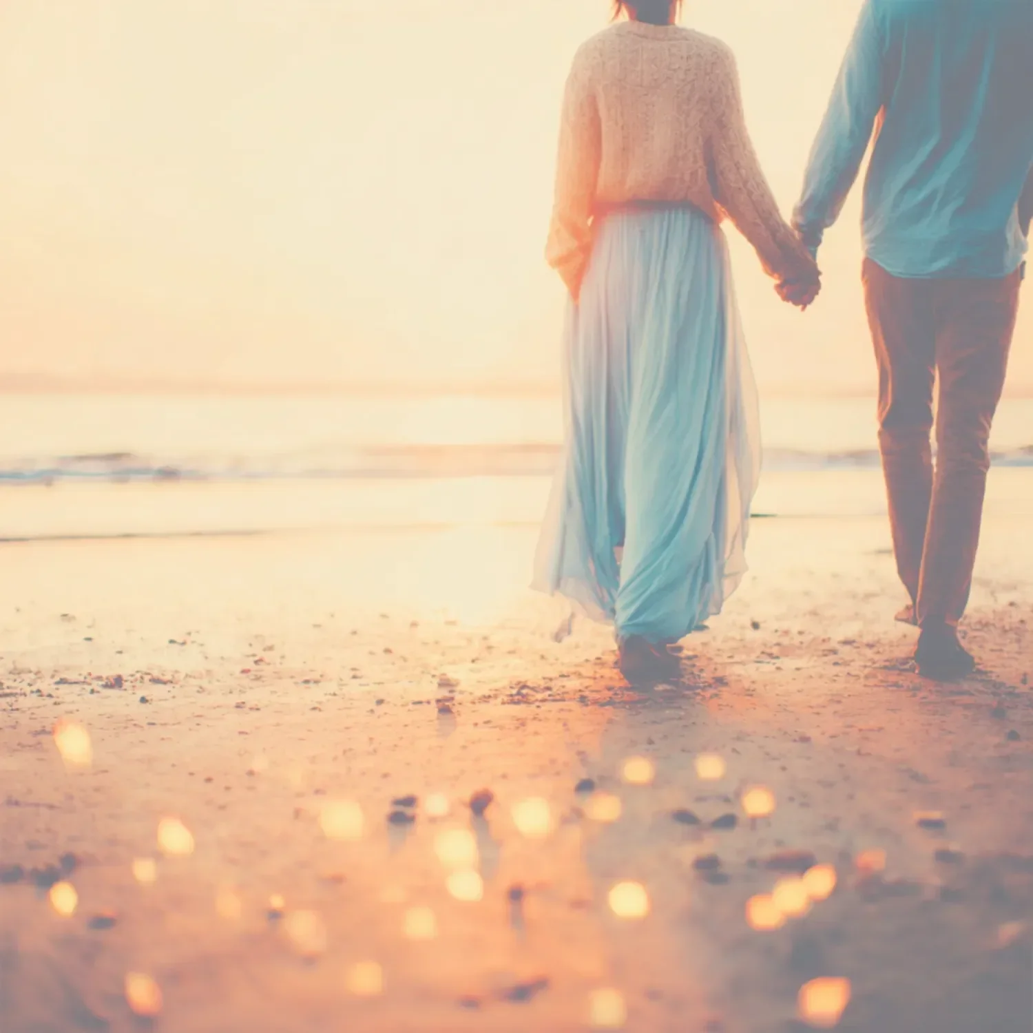 A couple holding hands and walking along the beach at sunset.